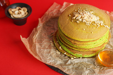 Tasty green pancakes with honey and nuts on color background