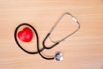 Red heart and stethoscope on wooden table. Doctor tool for heartbeat listening. Healthcare concept. Empty place for text,