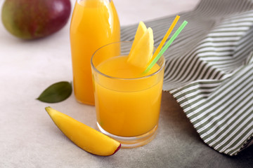 Glass and bottle of tasty mango juice on table