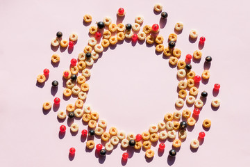 Whole grain cereal rings as circle on soft pink background. Healthy and Delicious breakfast. Top view. Copy space.circle of Breakfast cereal, corn flakes with berries.