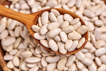 Uncooked white beans in a wooden spoon over the bowl of rice. Close up.