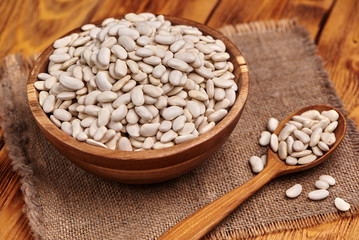 White beans a wooden bowl with the wooden spoon full of white beans, rustic background. Close up.
