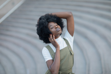 Beautiful African American girl with curly hair, fashionable overalls, and white turtleneck.