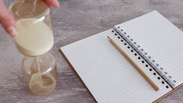 deadlines and productivity, hand placing hourglass next to notebok (speed up version)