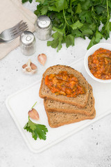 Bread with vegetable caviar on a white tray on a light gray background