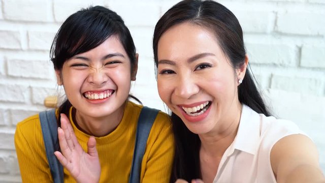 Happy Asian teenage daughter and middle-aged mother taking selfie or video calling