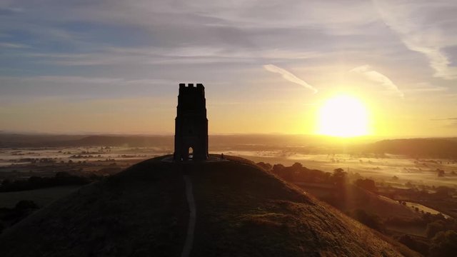 Aerial pan of the golden sunrise passing behind Glastonbury Tor, Somerset.