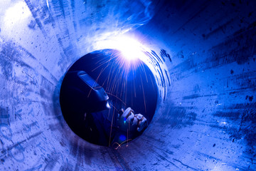 Welding of large pipes by industrial workers wearing safety equipment and dark glass to prevent...