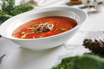 Macro Photo of Homemade Red Tomato Soup with Beef, Greens and Vegetables with Selective Focus. Rich Hot Veal Meat Broth with Tomatoes, Potatoes, Paprika in White Plate Close Up