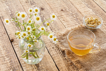 Glass cup of green tea and white chamomile flowers in a glass jar.