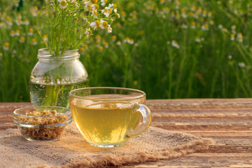 Glass cup of green tea with white chamomile flowers in a glass jar outdoor.