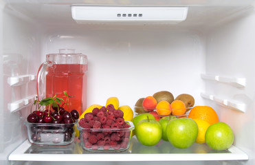 on the shelf of a white refrigerator, fresh fruit, berries and a glass jug with compote