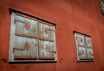 Geschlossener Fensterladen aus verwittertem Holz an roter Hauswand