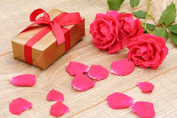 Gift box with rose flowers on the wooden background.