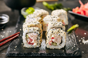 Macro shot of chicken uramaki sushi with bacon, processed cheese, tomato, green onion, black and white sesame, nori. Rainbow sushi rolls on natural black slate background with selective focus closeup