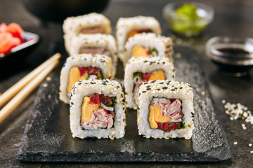 Rainbow uramaki sushi rolls with rice, bacon, processed cheese, tomato, green onion, sesame and nori on black slate plate background closeup. Macro shot of fusion maki sushi in Japanese restaurant