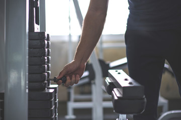 Handsome hand change weight on Iron heavy plates stacked of weight machine in gym