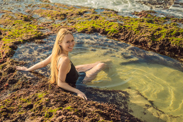 Young woman tourist on Pantai Tegal Wangi Beach sitting in a bath of sea water, Bali Island, Indonesia. Bali Travel Concept