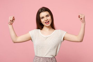 Strong young woman in casual light clothes posing isolated on pastel pink wall background, studio portrait. People sincere emotions lifestyle concept. Mock up copy space. Showing biceps, muscles.