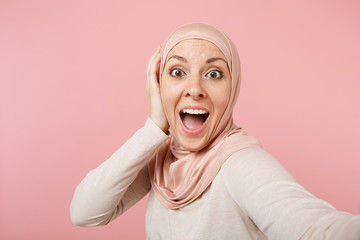 Close up excited surprised arabian muslim woman in hijab light clothes posing isolated on pink...