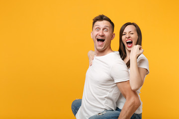 Naklejka premium Excited young couple in white t-shirts posing isolated on yellow orange background. People lifestyle concept. Mock up copy space. Giving piggyback ride to joyful sitting on back, doing winner gesture.