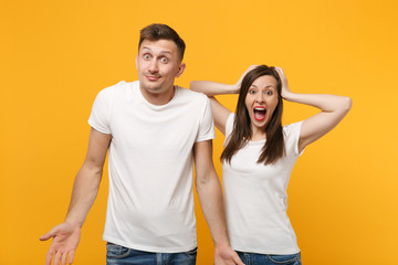 Fototapeta premium Young couple two friends guy girl in white empty blank design t-shirts posing isolated on yellow orange background. People lifestyle concept. Mock up copy space. Putting hands on head, spreading arms.