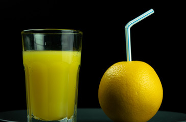 Orange yellow, which is inserted into a tube for drinks lies next to a glass of orange juice. Black background.