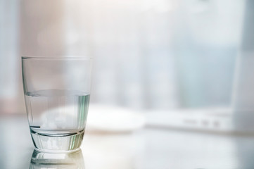 Closeup glass of clean water on white table with blurred image of laptop and mouse background.