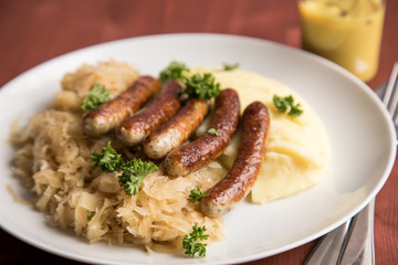 Kleine Bayrische Nürnberger Rostbratwürste mit Sauerkraut, Kartoffelpüree und Senf auf Holz Tisch Hintergrund