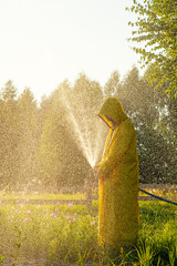 A young man in a yellow raincoat spraying a green lawn from a hose spraying water