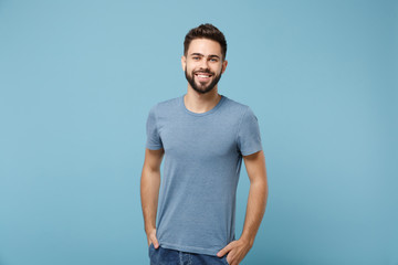 Fototapeta premium Young smiling handsome man in casual clothes posing isolated on blue wall background, studio portrait. People sincere emotions lifestyle concept. Mock up copy space. Holding hands in pockets.