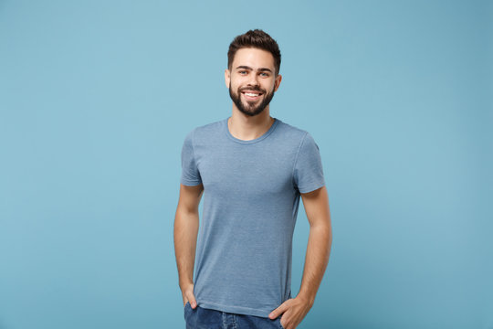 Young smiling handsome man in casual clothes posing isolated on blue wall background, studio portrait. People sincere emotions lifestyle concept. Mock up copy space. Holding hands in pockets.