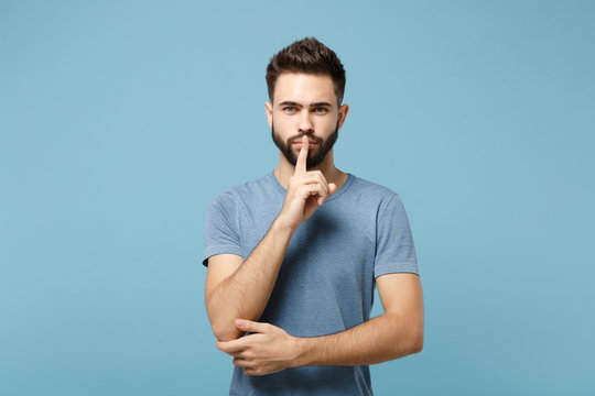 Young man in casual clothes posing isolated on blue wall background, studio portrait. People sincere emotions lifestyle concept. Mock up copy space. Say hush be quiet with finger on lips shhh gesture.