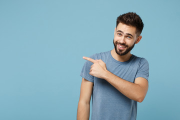 Young attractive smiling funny man in casual clothes posing isolated on blue background, studio portrait. People sincere emotions lifestyle concept. Mock up copy space. Pointing index finger aside.