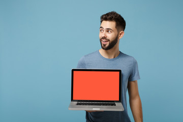 Young attractive man in casual clothes posing isolated on blue wall background in studio. People lifestyle concept. Mock up copy space. Hold laptop pc computer with blank empty screen , looking aside.