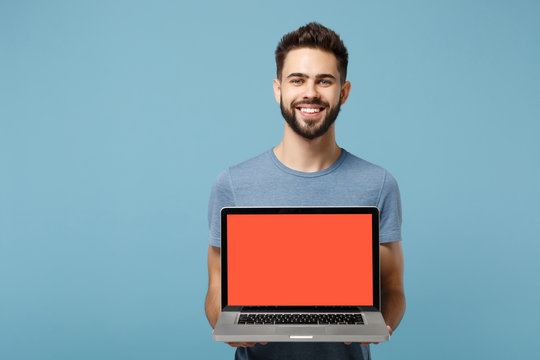Young smiling handsome man in casual clothes posing isolated on blue wall background in studio. People lifestyle concept. Mock up copy space. Hold in hands laptop pc computer with blank empty screen.