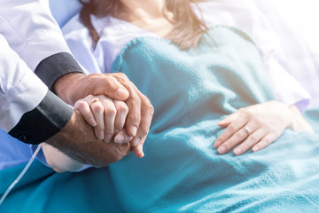 Male doctor holding female patient hand on the hospital bed. - obrazy, fototapety, plakaty