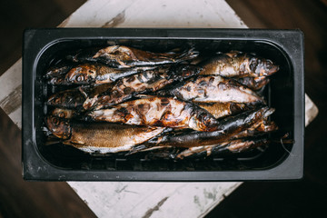 Smoked herrings in black box on wooden background with copy space