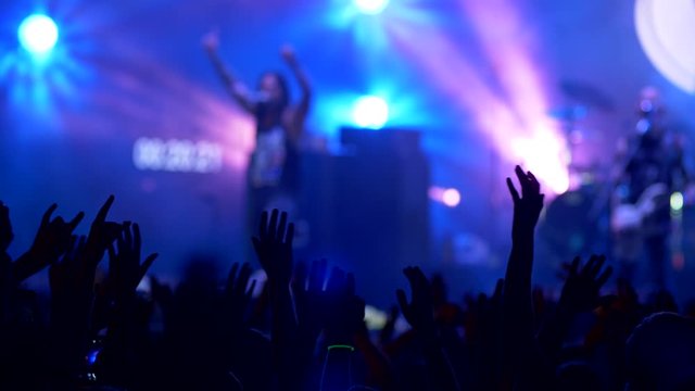Crowd of people waving their hands in rythm of song on a rock concert. People as silhouette. Stage shining with blue color. Unrecognizable Singer and guitarist performing. 4K