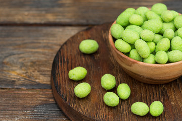 Roasted peanuts in wasabi in a wooden bowl on a wooden table