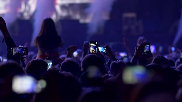 Fires lighting, flashes blinking and smokes coming out during show on rock concert. Spectators watching show and shooting videos with their smartphones. Blue light. 4K