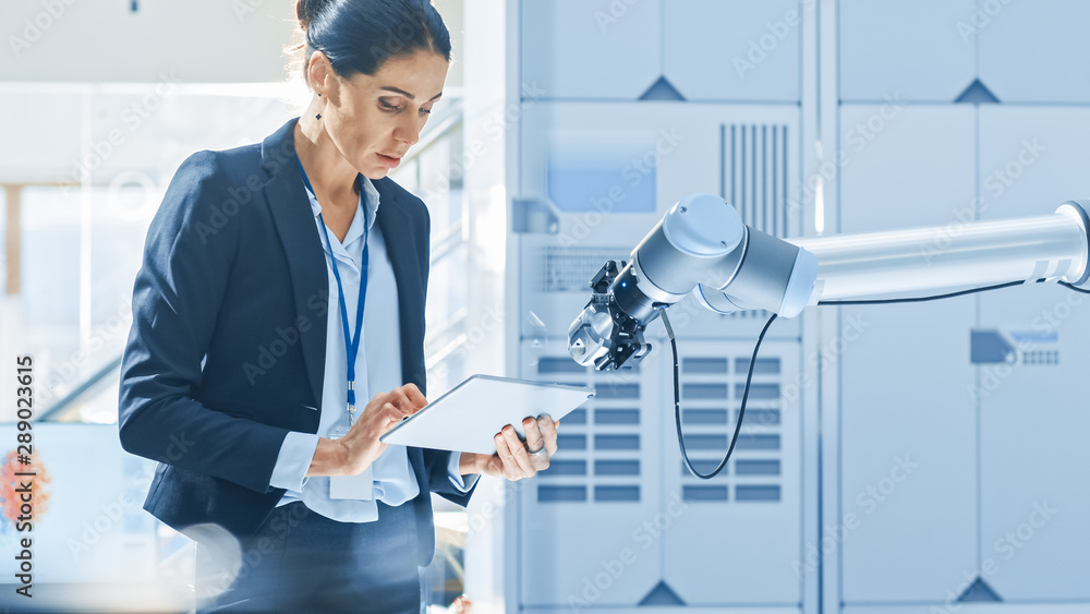 Leinwandbilder Stylish Female Industrial Robotics Engineer Uses Tablet Computer to Program and Manipulate Robot Arm for Lifting, Moving Objects. Technology Research Facility for Machine Learning and Cloud Computing