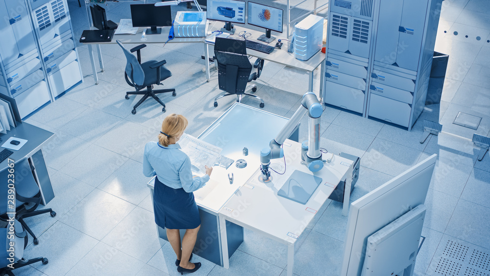 Poster Stylish Female Industrial Robotics Engineer Looks at Blueprints Engineering Ways to Program and Manipulate Robot Arm for Lifting, Moving Objects. Technology Research Facility for Machine Learning