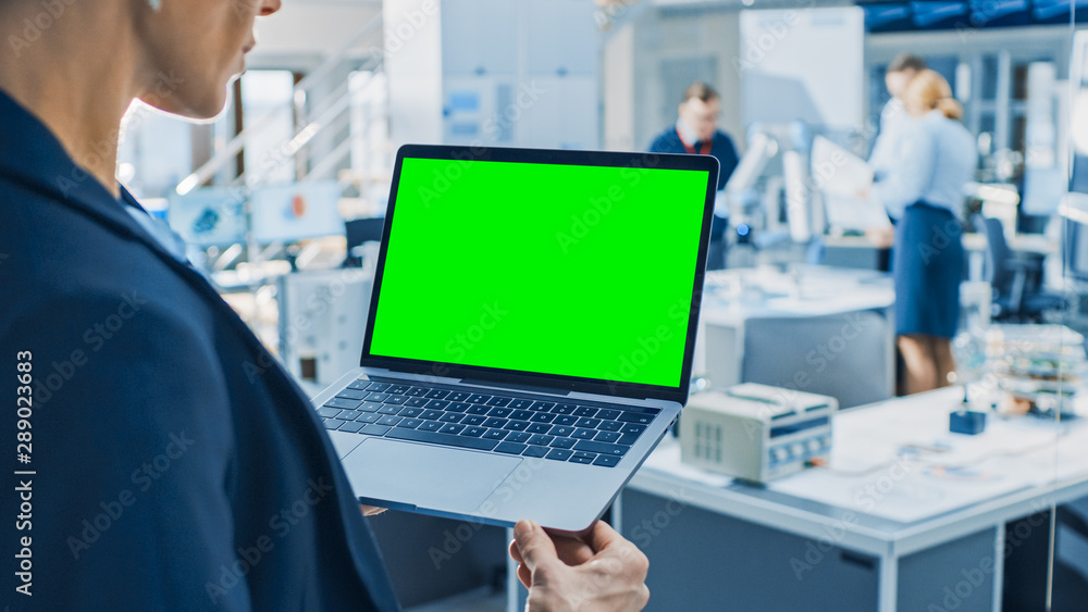 Leinwandbilder Engineer Holds Green Mock-up Screen Laptop Computer. In the Background Team of Industrial Engineers Working with Functional Robot Arm in Modern Bright Research Facility