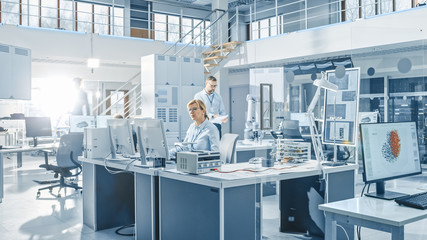 Senior Female Chef Engineer Working on Computer, Programming Robot Arm in Bright Modern Industrial Robotics Technology and Design Office. Technologically Advanced Research Facility.