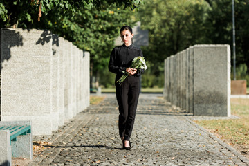 sad woman holding flowers and walking in graveyard