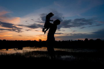 Silhouette man throws up girl field in the evening. Concept to build relationships within the family.