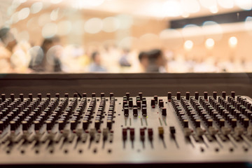 Close up buttons of black audio mixer board console. Music equipment in sound audio room with abstract blurred seminar for business meeting in conference hall.