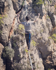 A man is walking along a stretched sling. Highline in the mountains. Man catches balance....