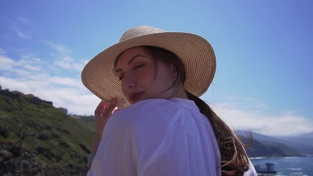 Cute young hipster woman posing for the camera, standing on the edge of a cliff above the Atlantic Ocean. Model on the island of Tenerife, Spain